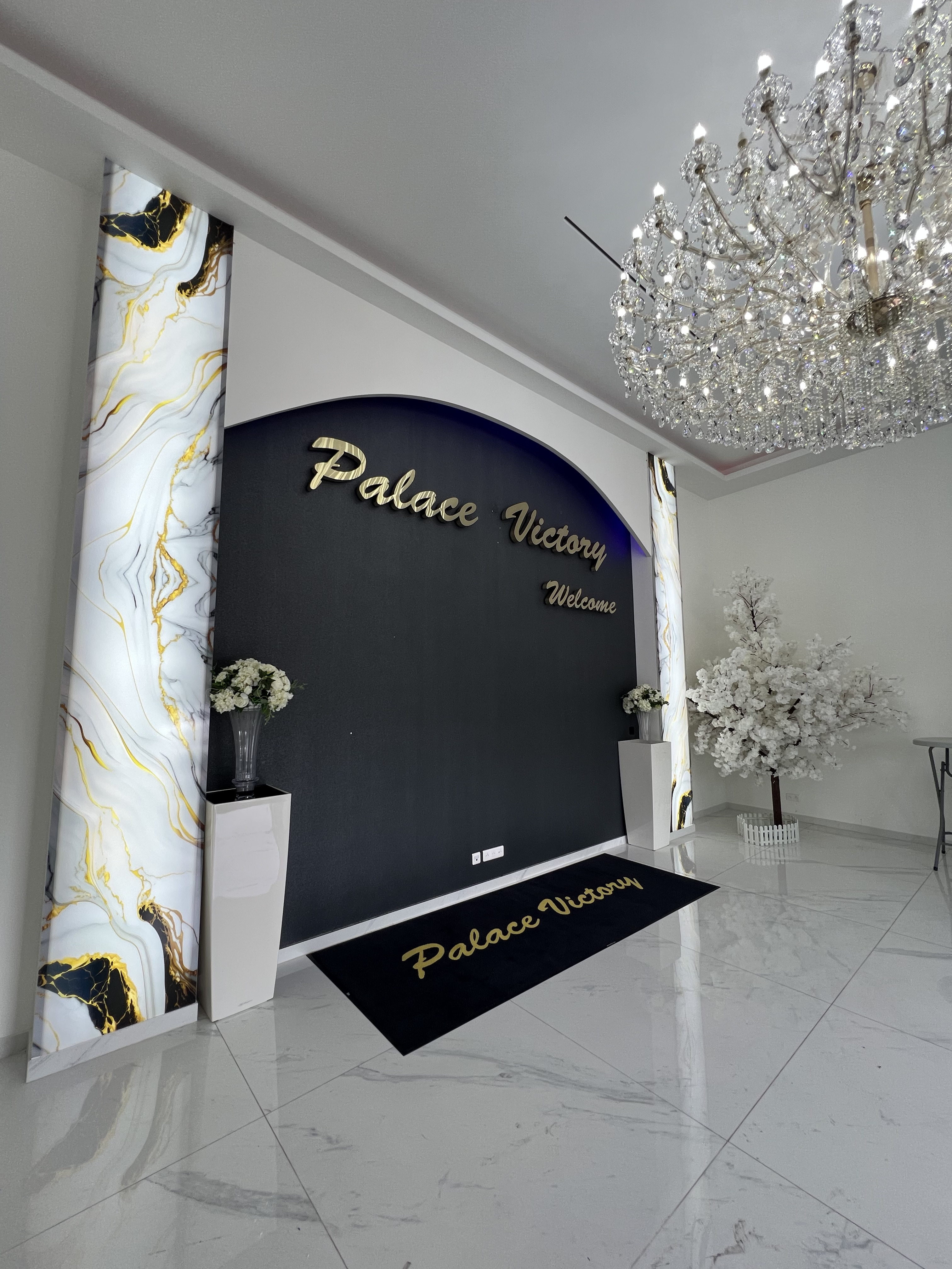 Hall d'accueil du Palace Victory Events - Mur d'entrée doré, colonnes marbrées, lustre en cristal et cerisier blanc